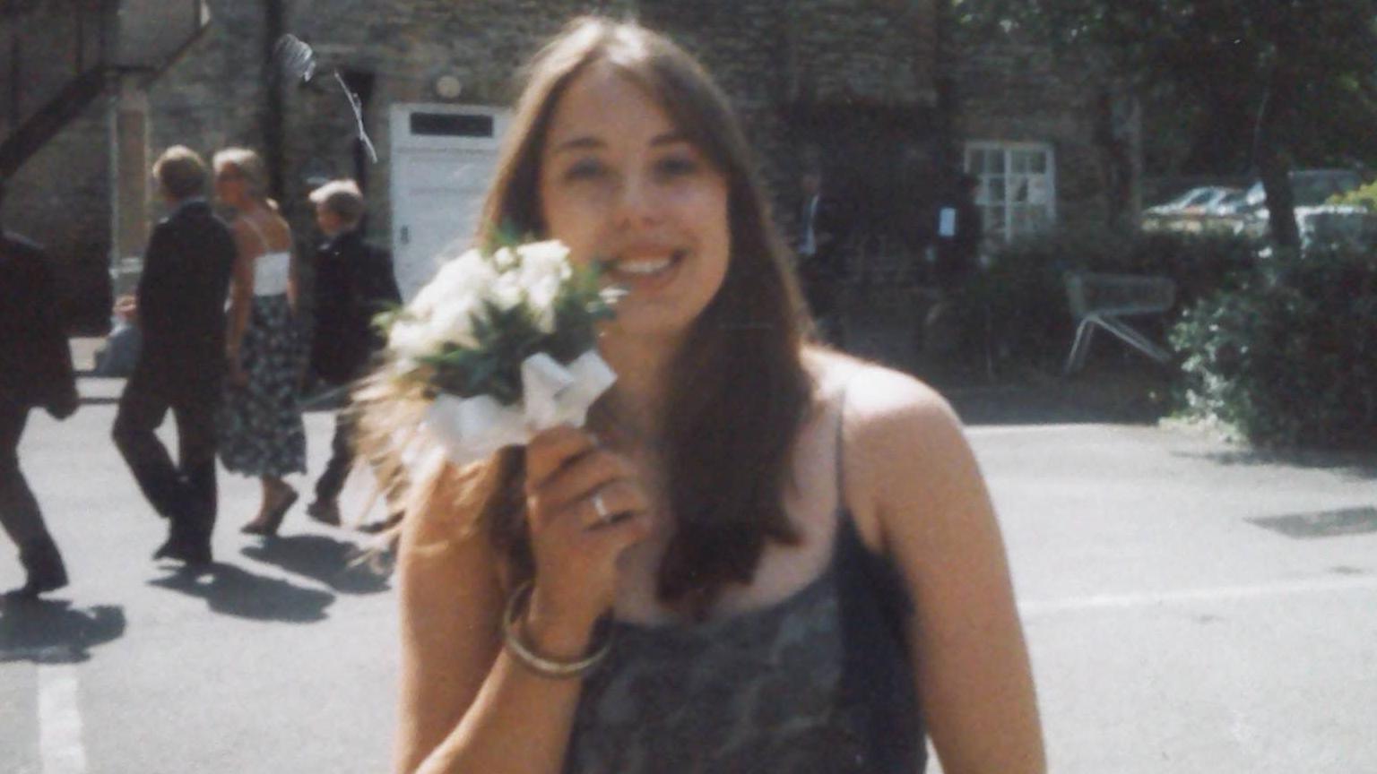 A picture of a smiling young woman with long brown hair - she is holding a posy of white flowers. 