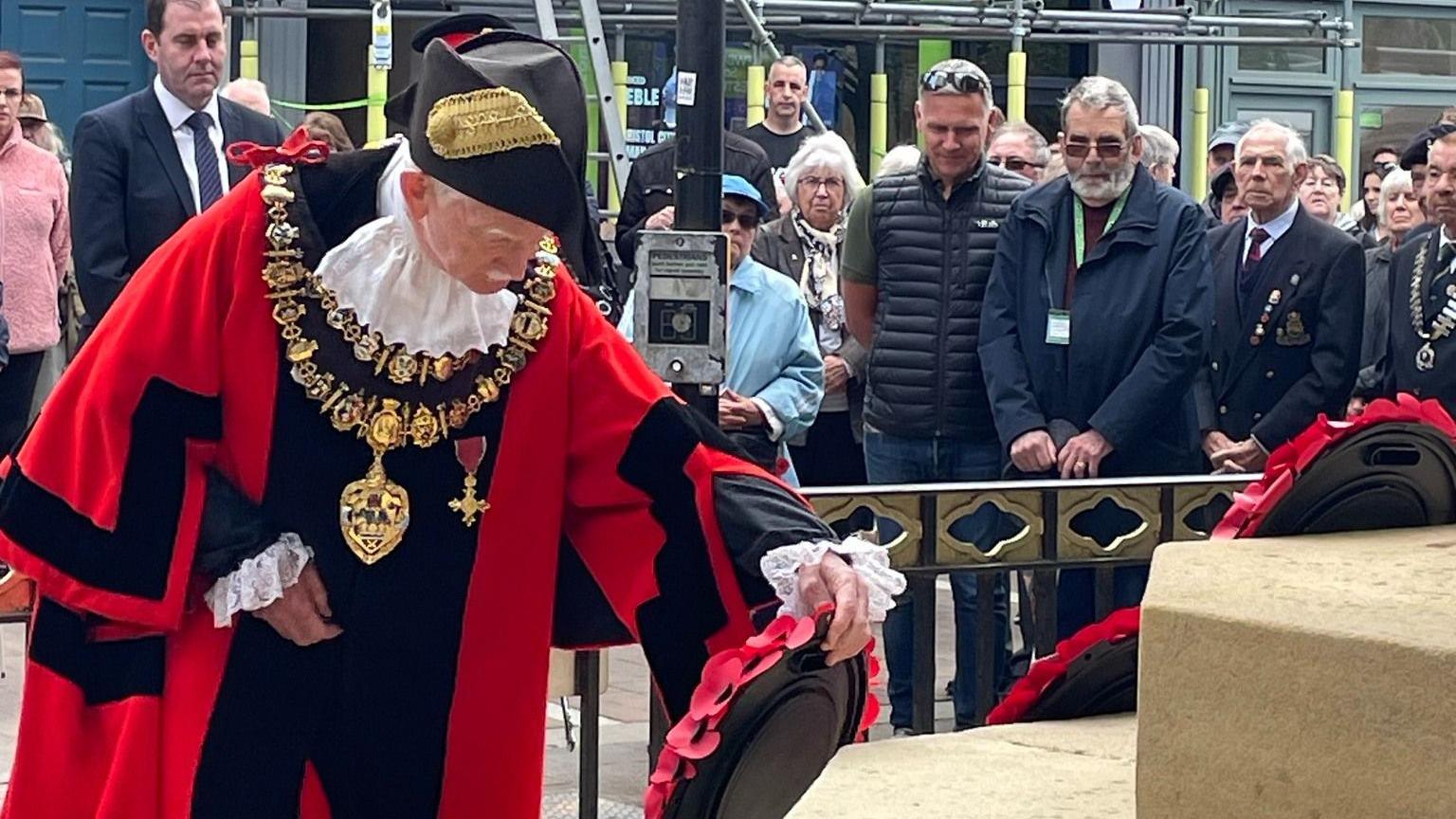 Newbury's mayor in his ceremonial red robes laying a wreath as onlookers gather in the background