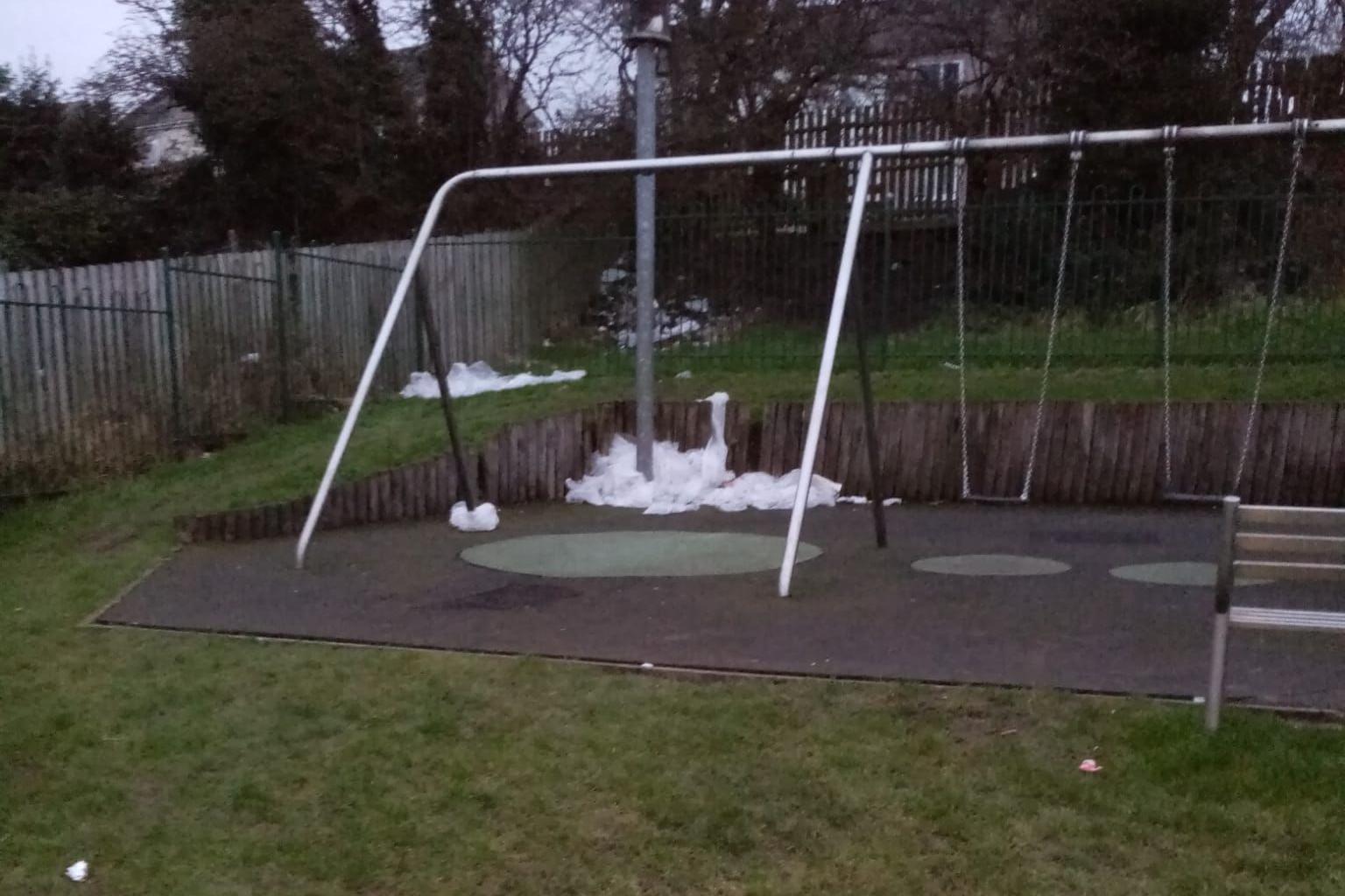 A metal pole behind a swing set has a mound of white plastic bags at the bottom.