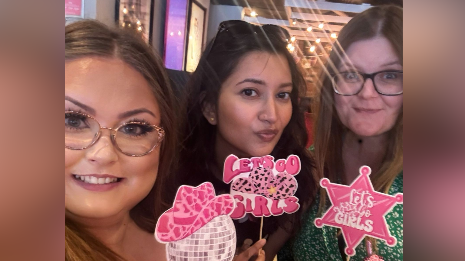 Heather Cowell takes a selfie with two other women. The hold small pictures on sticks that read Let's Go Girl.