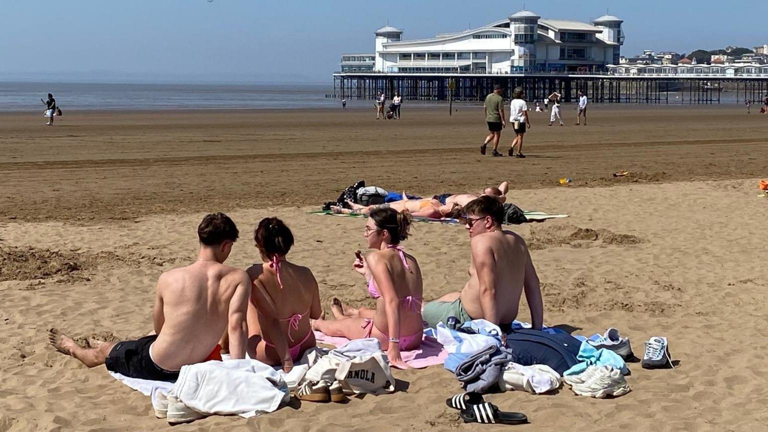A group of four young people with their backs to the camera sunbathe on the beach at Weston-super-Mare in Somerset