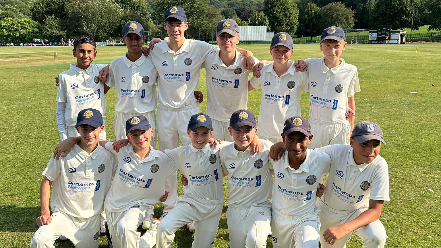 12 boys dressed in cricket whites and caps