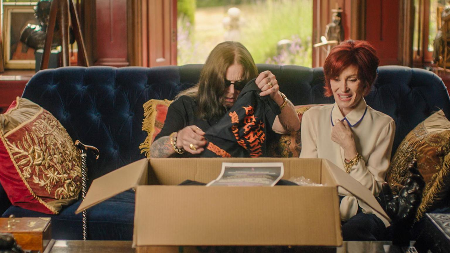 Ozzy and Sharon Osbourne sat on the couch of their home in England, looking at final gig merchandise from a cardbox box placed on the table in front of them