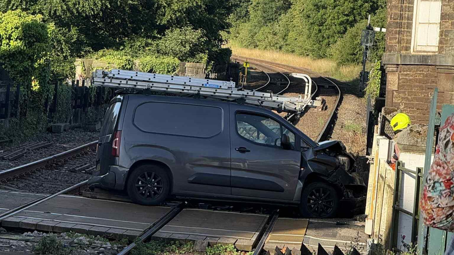 A dark grey van which has crashed into a level crossing. The bonnet of the van is smashed.