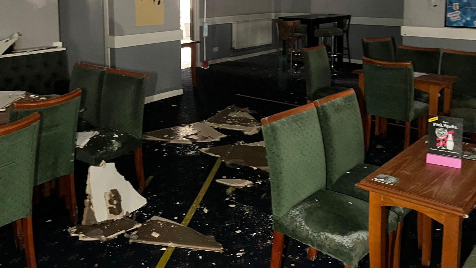 Broken ceiling panels on the floor of a community centre in Yate, with green chairs and tables covered in dust.