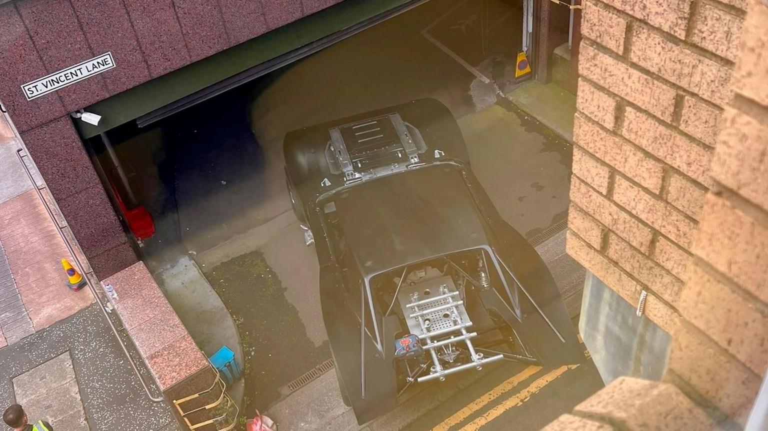 The Batmobile - a souped up black car - driving into a car park.