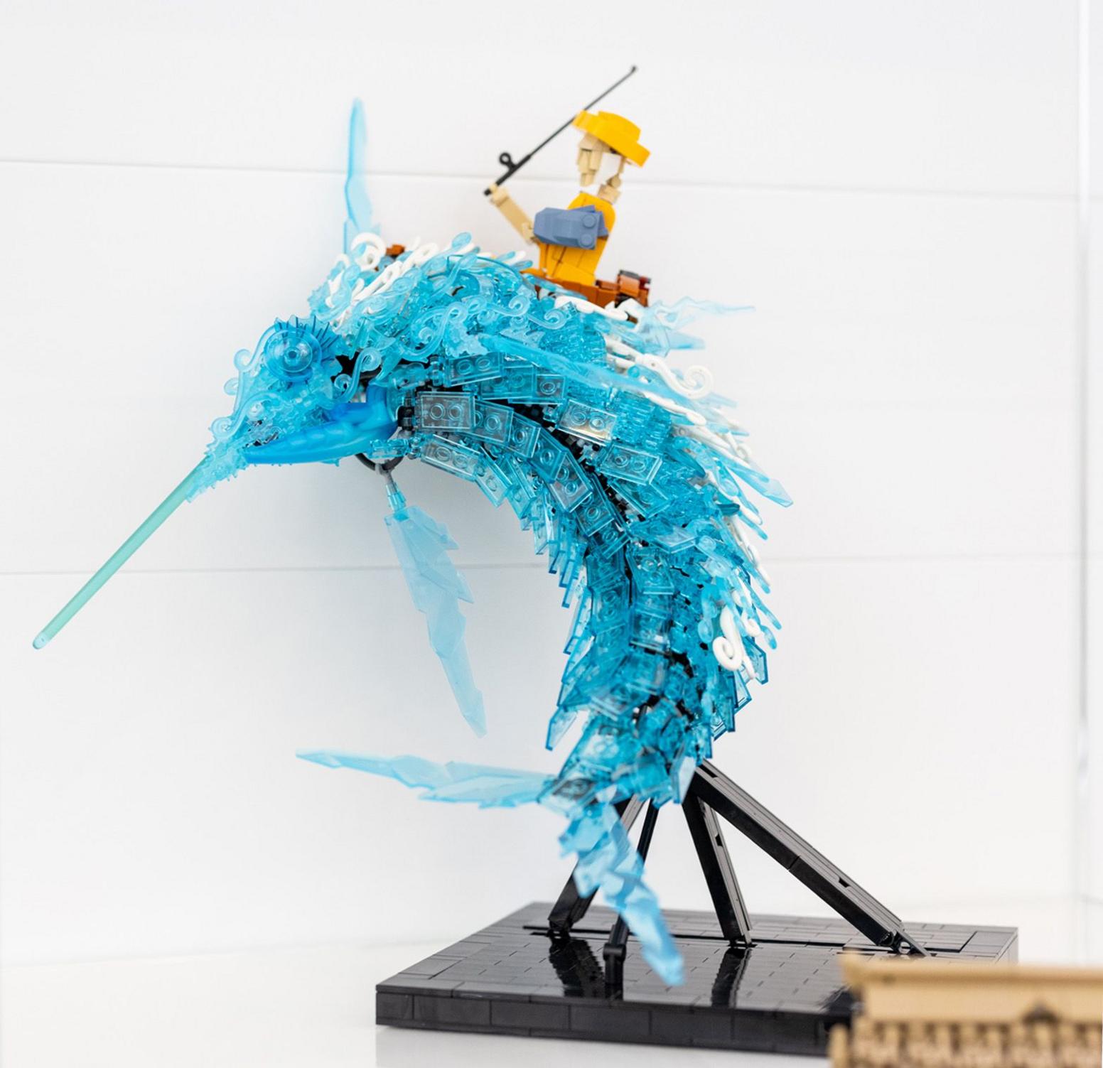 The Old Man and the Sea Lego model depicts Santiago trying to catch a giant translucent blue marlin. It is mounted on a black stand.