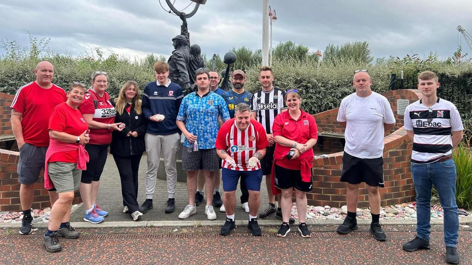 A group of people outside Stadium of Light, each wearing a different colour-ed football shirt