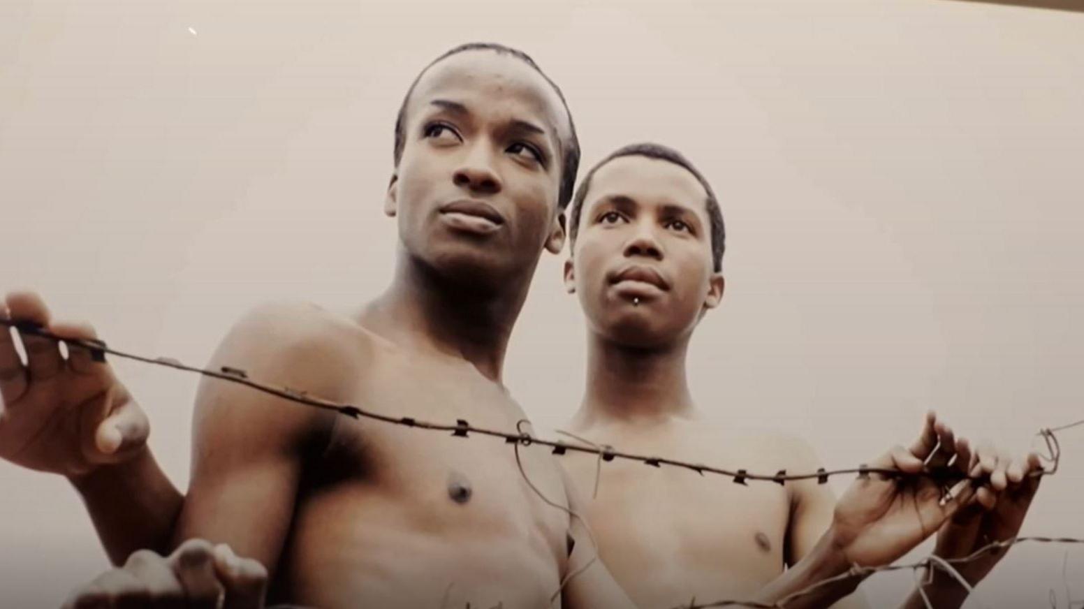 Image of two men in front of barbed wire