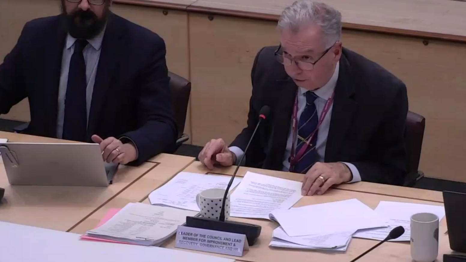 Dexter Smith, who has white hair and glasses, is sat at a table during Monday's council meeting. The picture is taken from the video of the council's meeting.