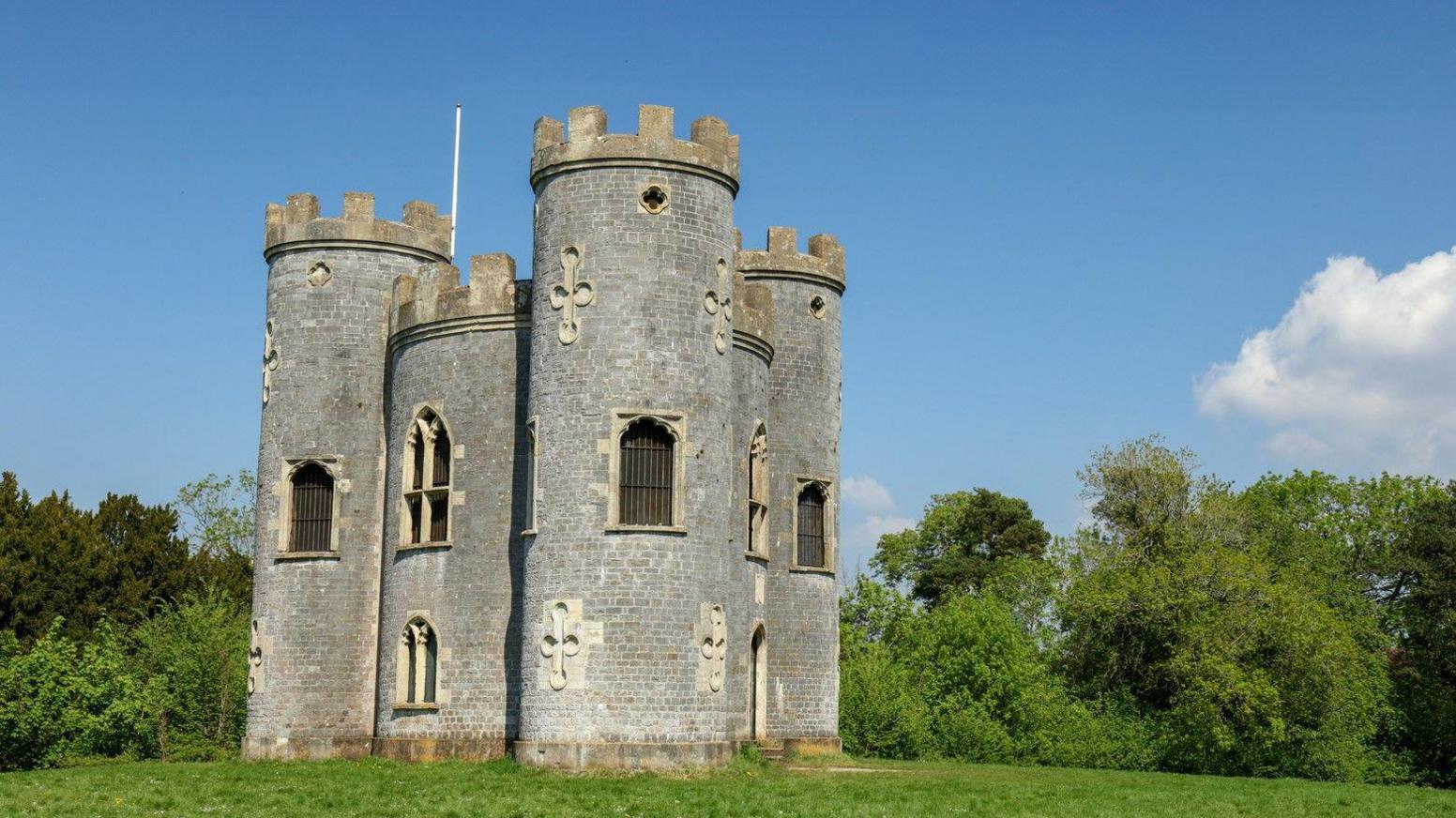 Blaise Castle in Bristol under a blue sunny sky with green grass and trees around it