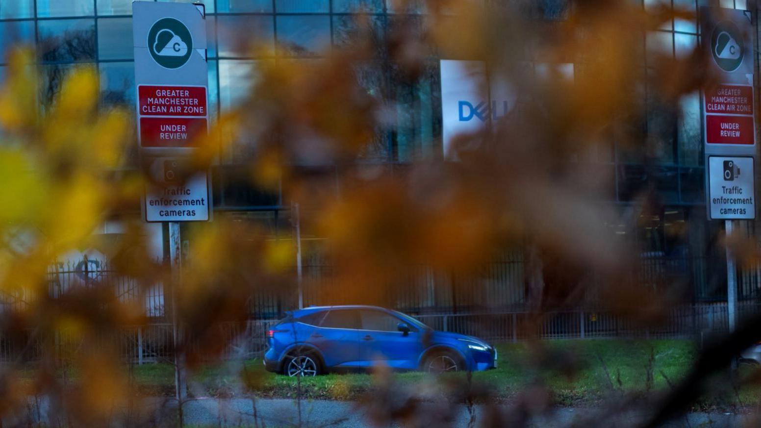 Signs advising motorists about traffic cameras are seen through some trees at the entrance to the proposed clean air zone in Manchester.