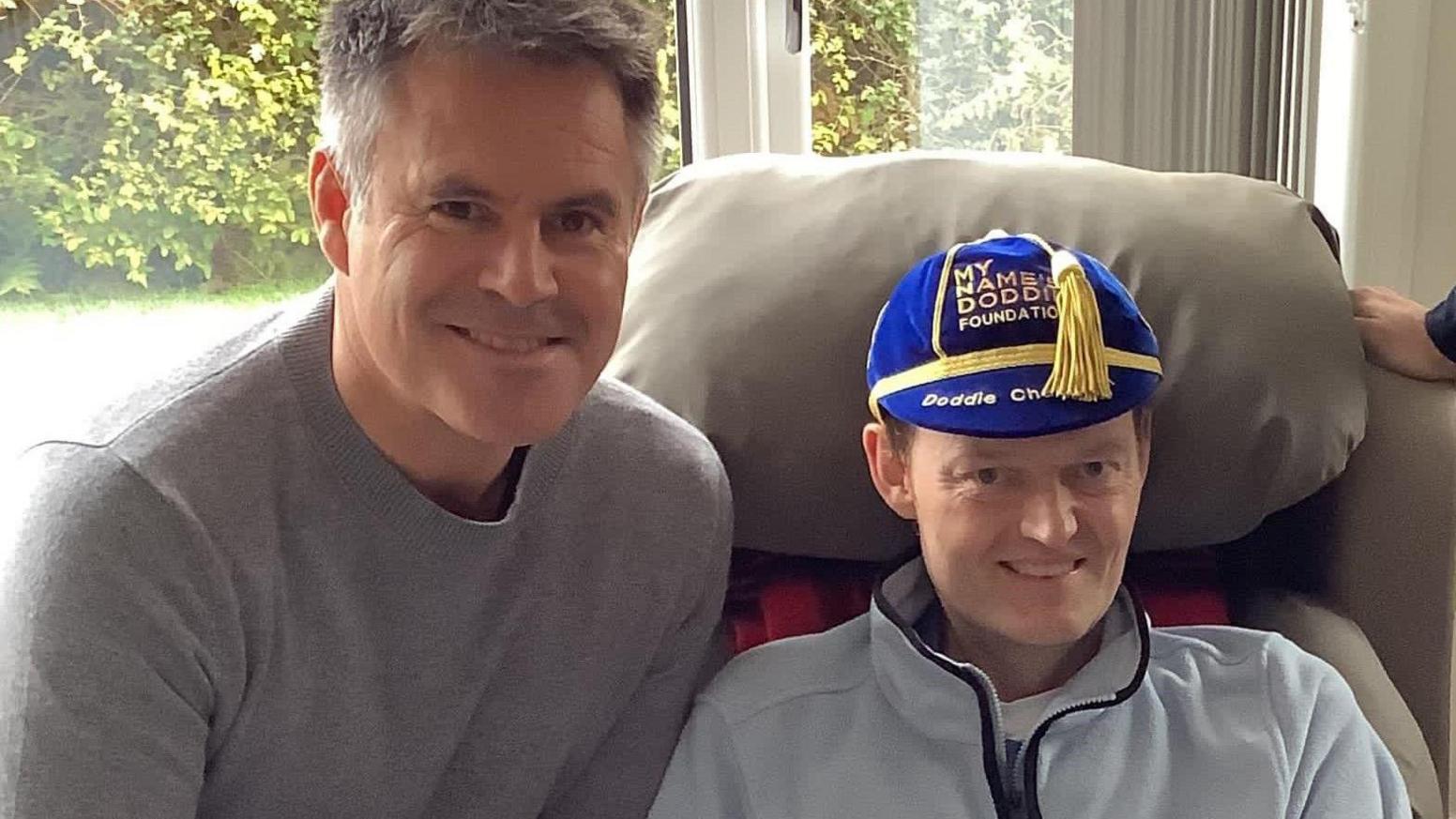 Kenny is on the left and is wearing a grey jumper. Scott is smiling at the camera and is wearing a yellow and blue hat with a tassel.