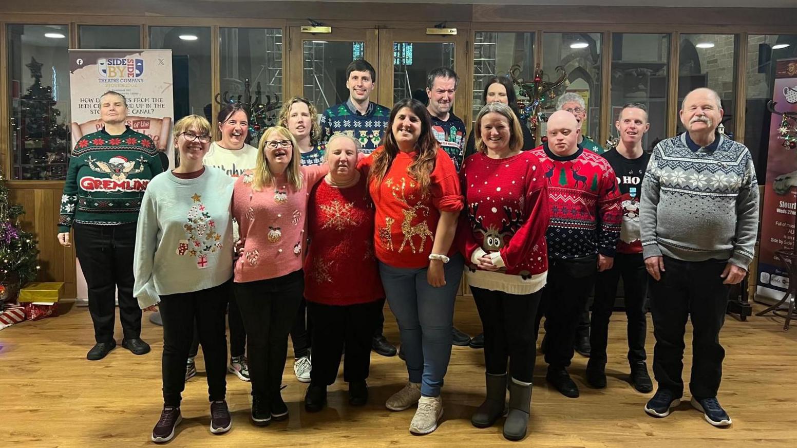 A group of men and women standing together and wearing an array of Christmas jumpers