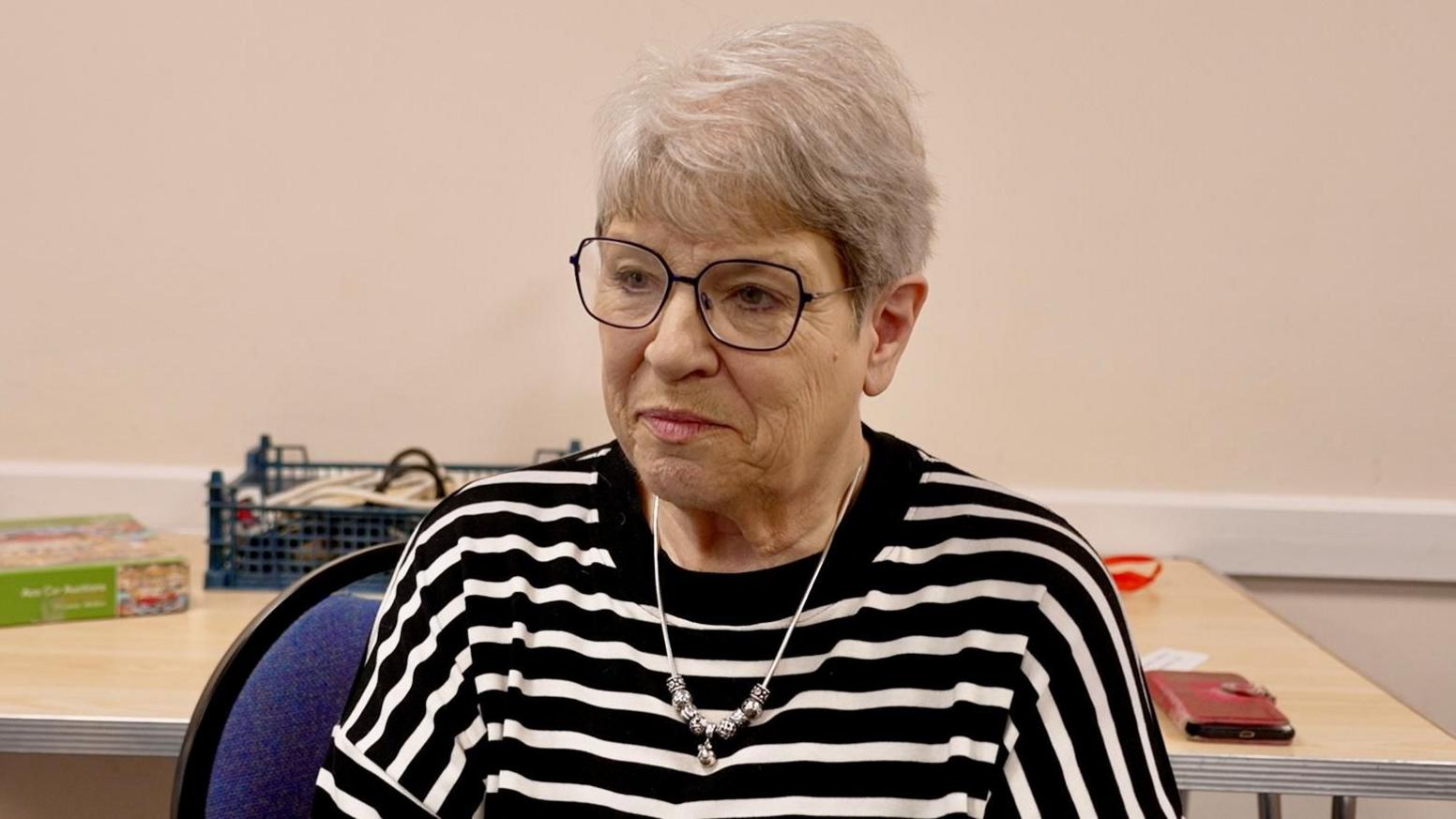 Diana Johnson has white hair, glasses and a black and white stripey top.