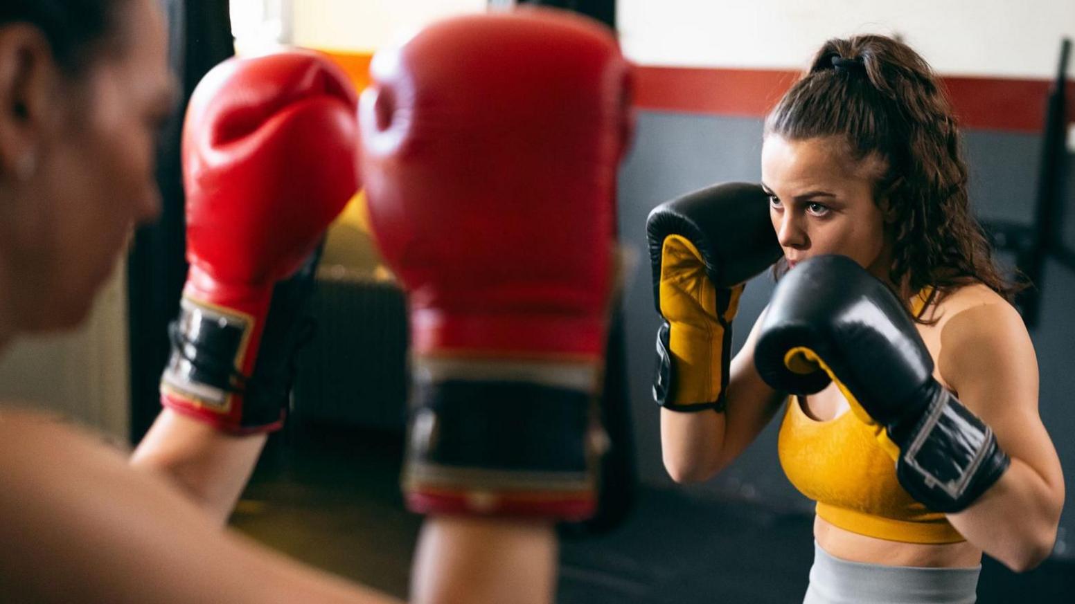 A young female kickboxer sparring with a female coach, during kickbox practice in the gym