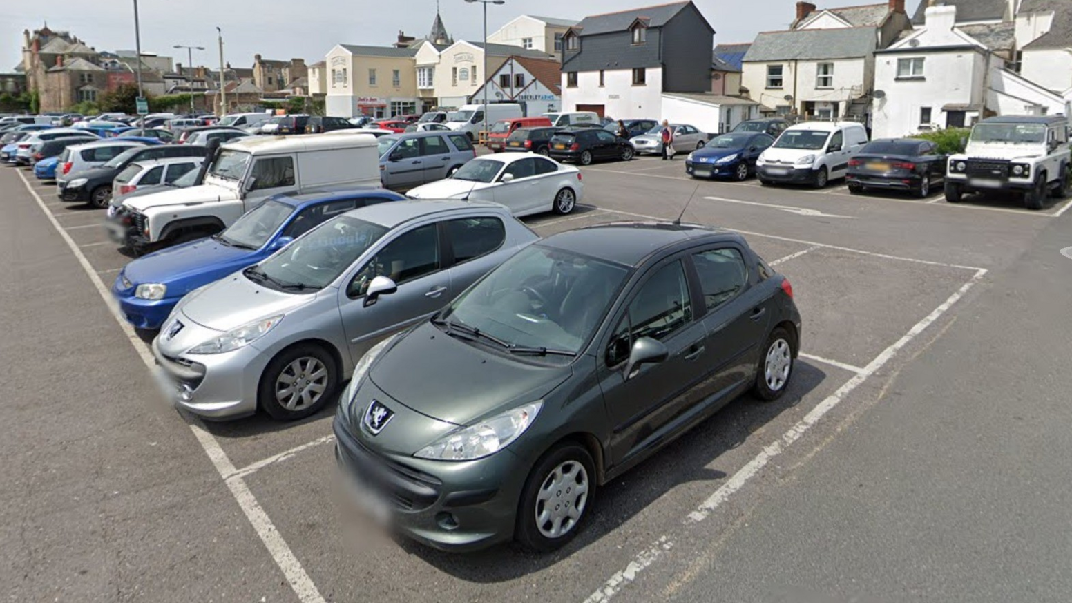 Numerous vehicles of different colours parked in a car park.