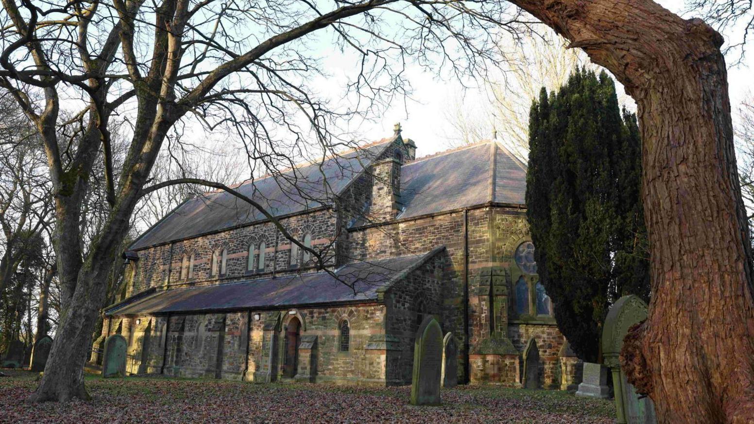 St John's church in Killingworth. The stone building sits in the grounds of an old cemetery with trees and fallen leaves on the ground.