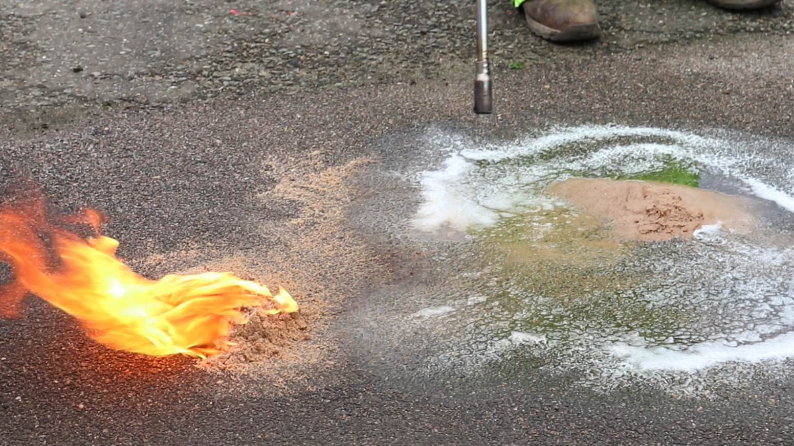 A mound of sand on the road is on fire, to the right is a pool of foamy liquid