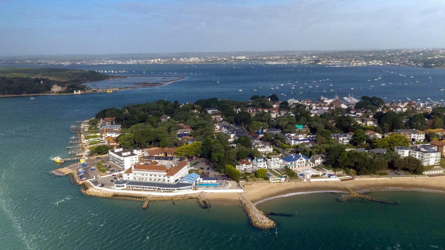 Aerial view of the Sandbanks peninsula with large houses, mature trees and sandy beaches. Poole Harbour is in the background.