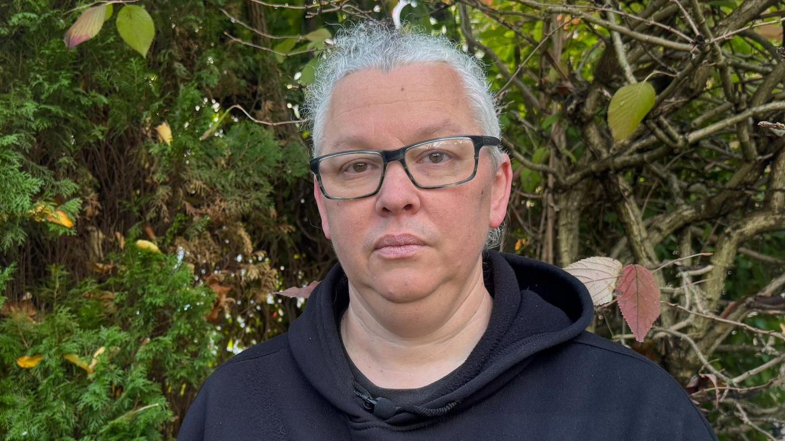 Graham Caisley wears a sombre expression as he faces the camera. He has white hair and glasses and wears a dark hoodie.