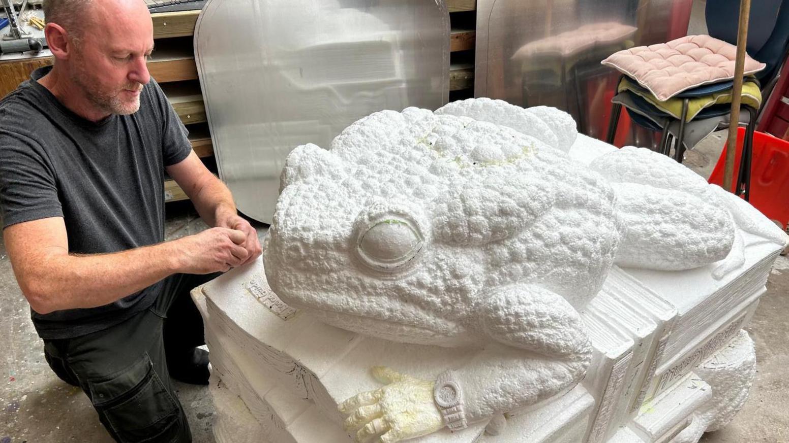 A man kneels down next to a large polystyrene model toad.