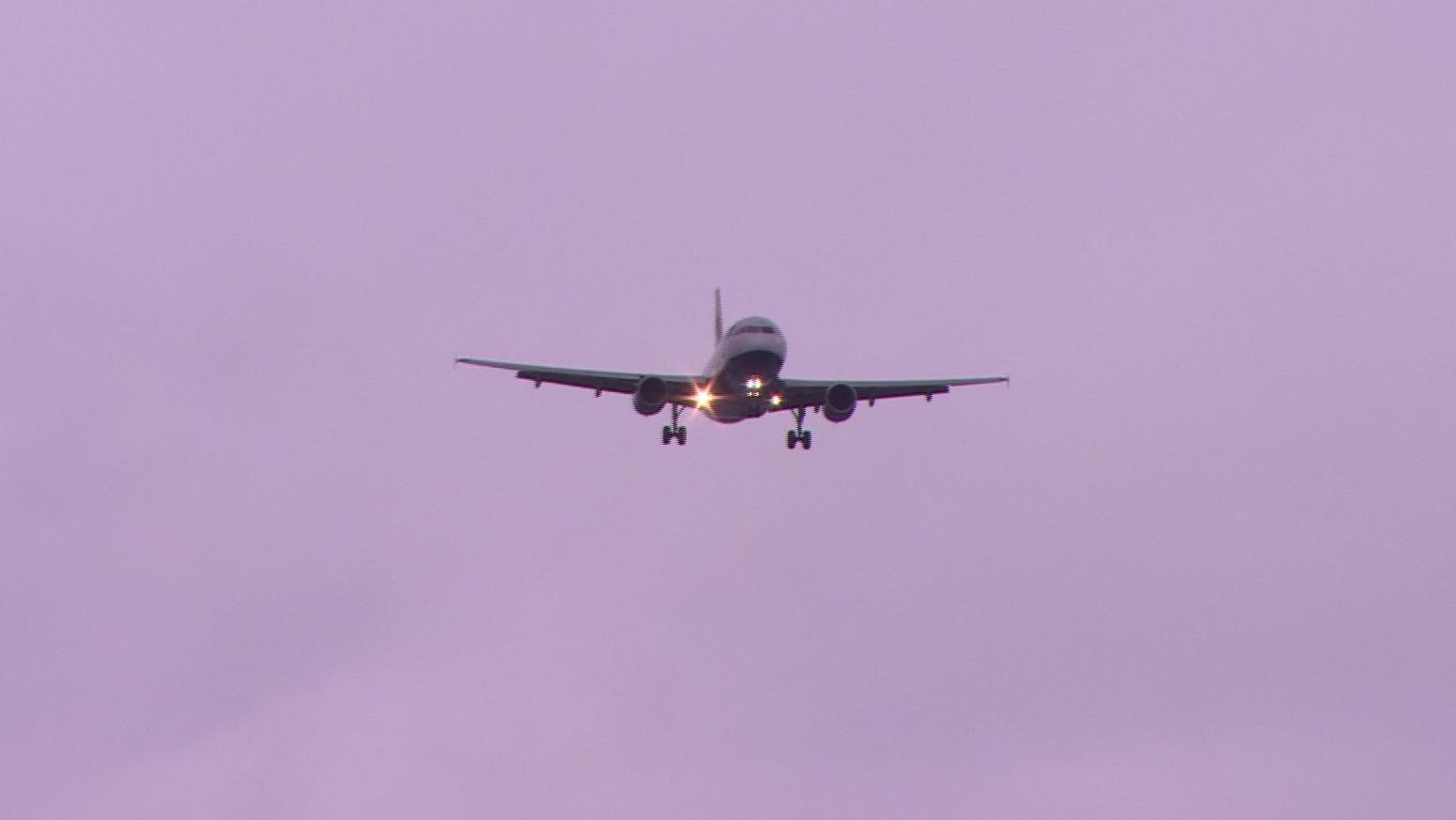 A plane with lights on coming into land with a grey sky behind it