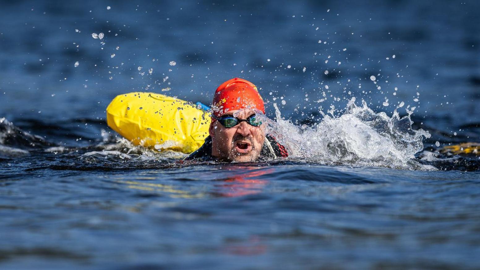 A swimmer attached to a yellow float and they are splashing as they swim