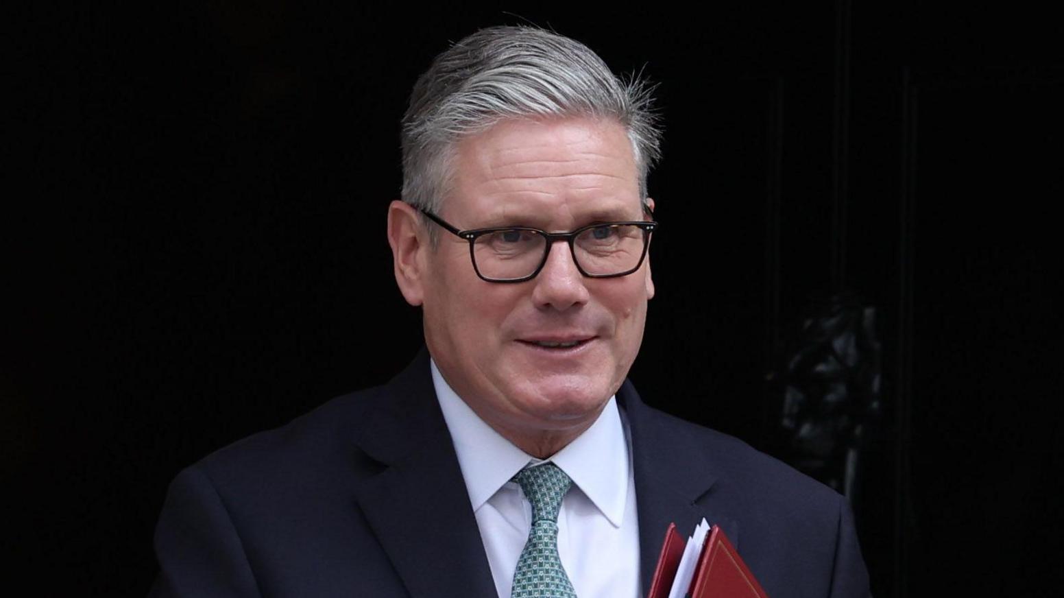Sir Keir Starmer in front of the black door of 10 Downing Street holding a red folder.