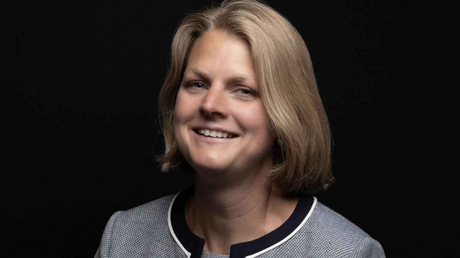 Abi McGuire smiling in a grey suit against a black screen