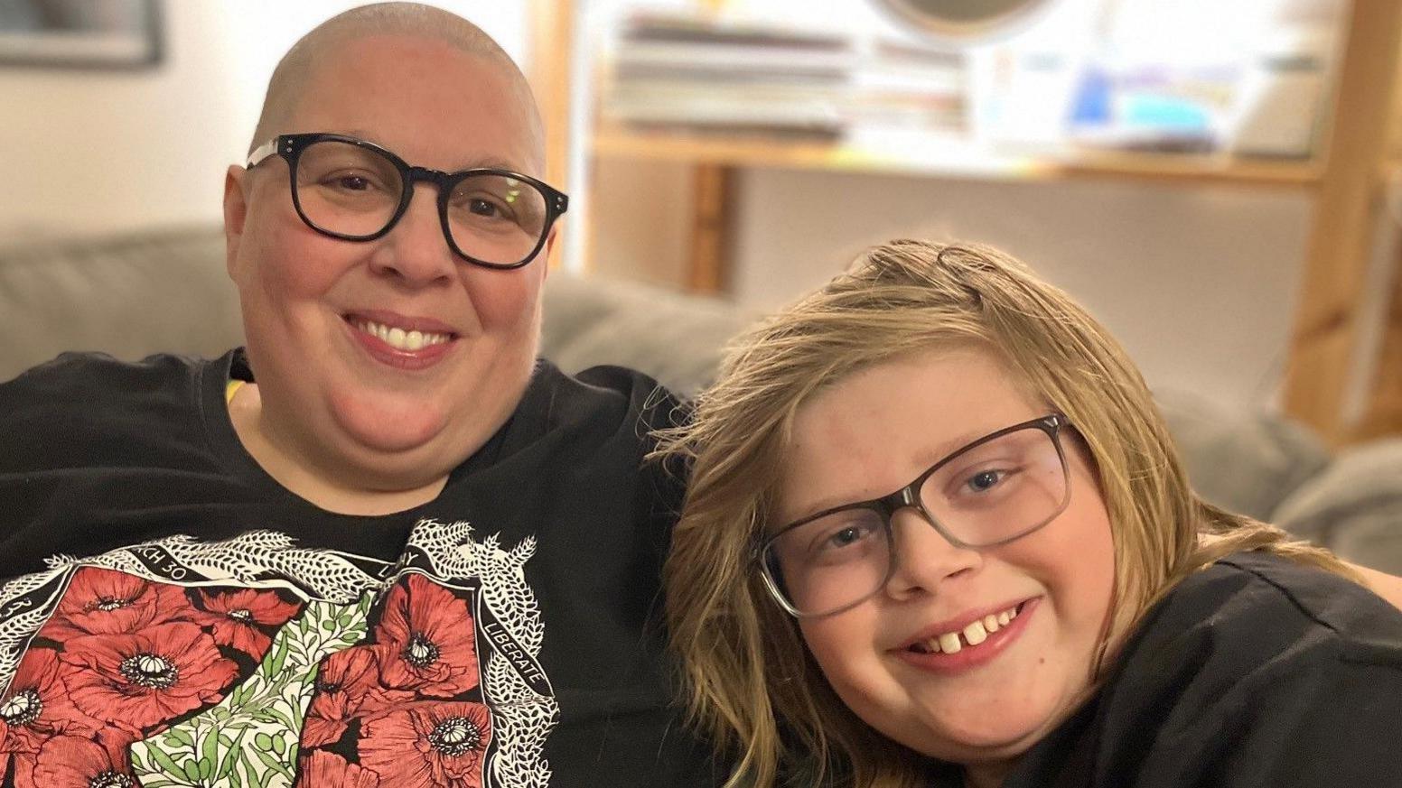 A person on the left has their arm around the shoulders of a boy on the right. Both of them are smiling.