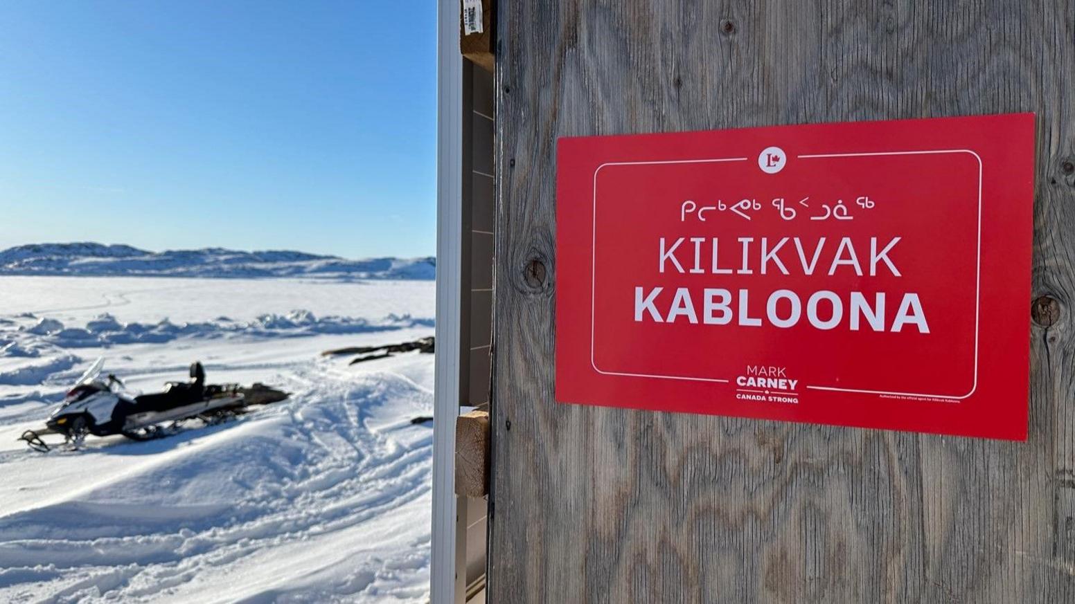 A campaign sign for Kilikvak Kabloona with snow and a snowmobile in the background