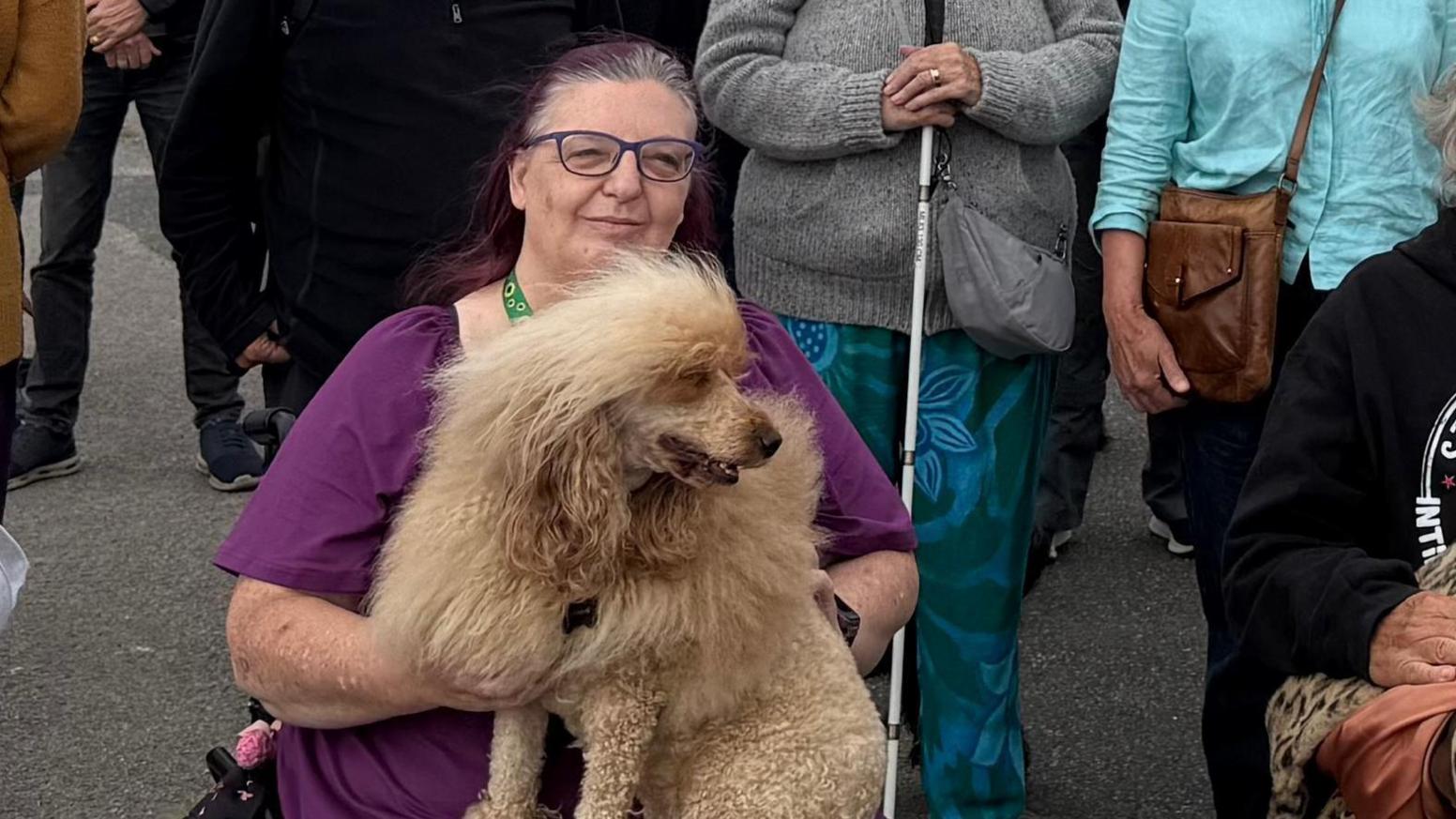 Chantelle Rea-Bradley, who is sitting on a mobility aid and holding a poodle on her lap. She is seated in front of a group of other protesters.