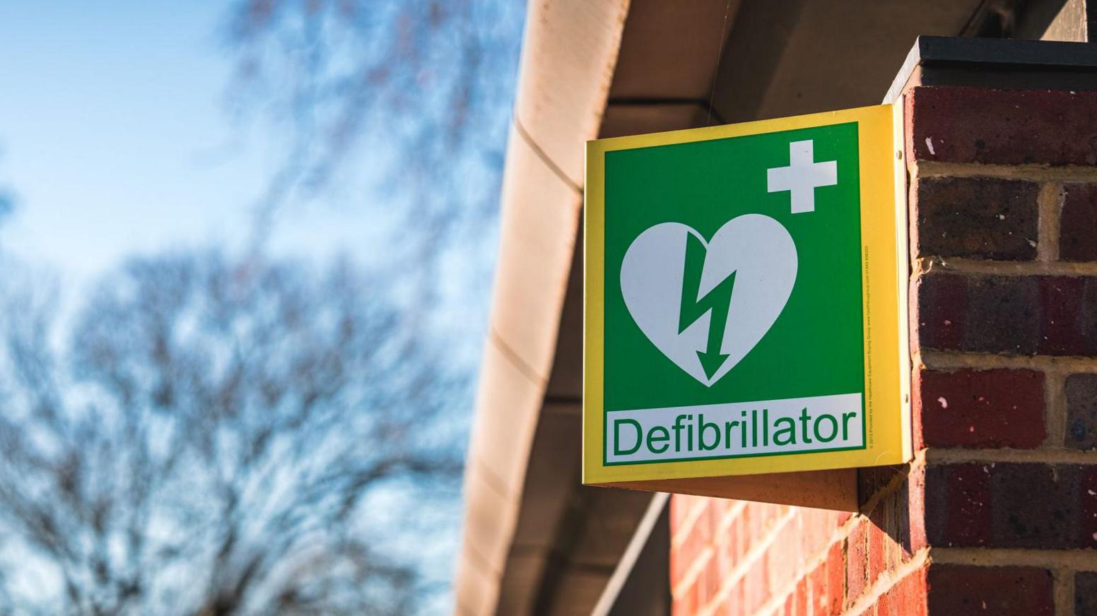 A general view picture of a sign for a defibrillator, with green writing on a yellow sign.