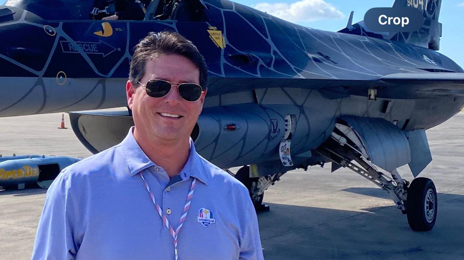 Fred Lopez standing in frong of a combat jet, dressed in civilian clothes