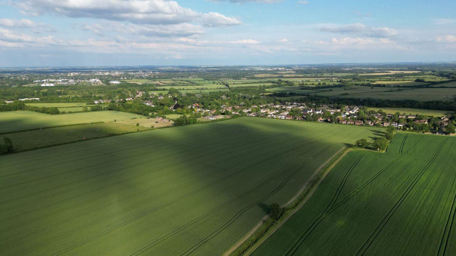 An aerial view of green fields with small residential settlements visible in the distance. 