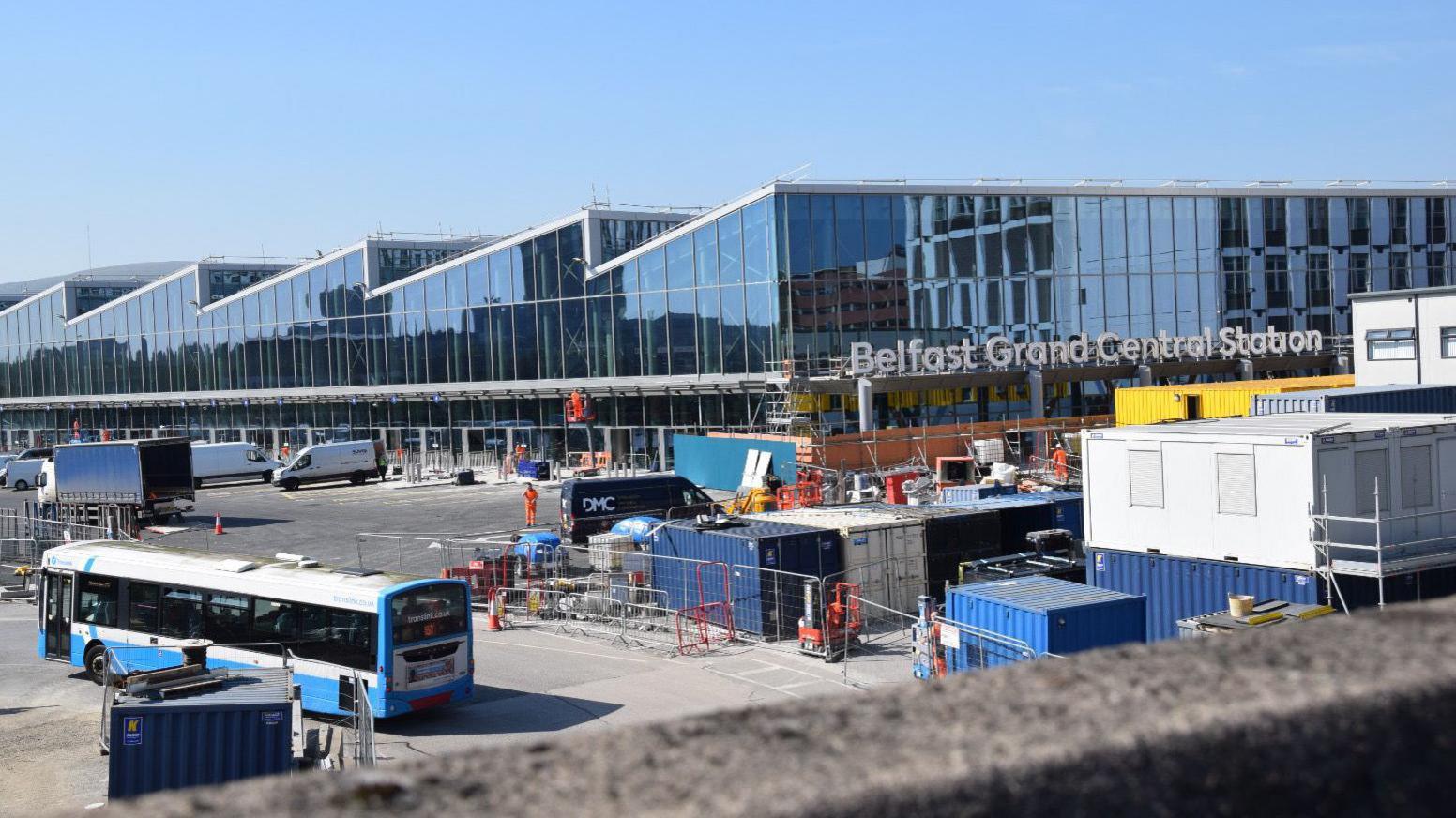 The new Belfast Grand Central Station building with parts under construction. An Ulsterbus drives along the side of a building site within the grounds of the new station.