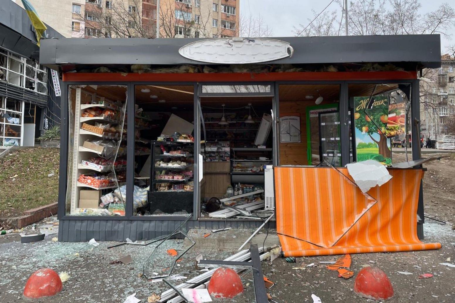 A bakery stands with shattered windows in Kyiv. Broken glass and debris litter the pavement in front of it.