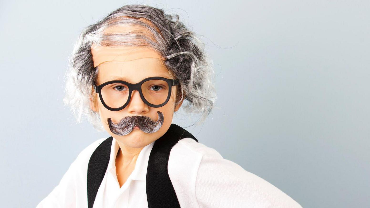 Boy dressed in white shirt and black waistcoat with grey wavy hair wig and glasses with grey moustache.