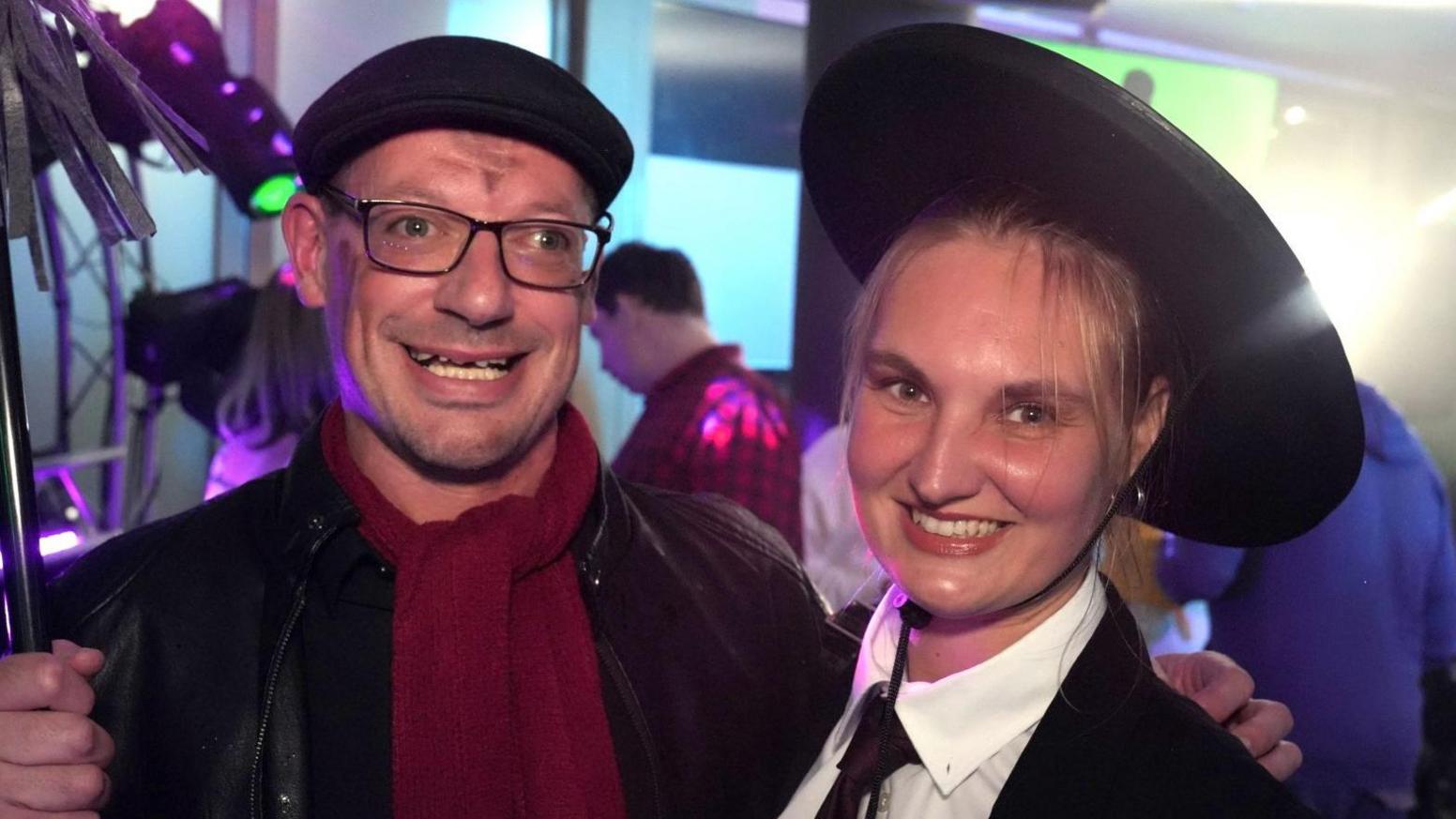 Chris, who is dressed as Bert from Mary Poppins, stands with his arm around his fiancee Faye, who is dressed as Mary Poppins. They are on a dance floor surrounded by flashing lights and other dancers.