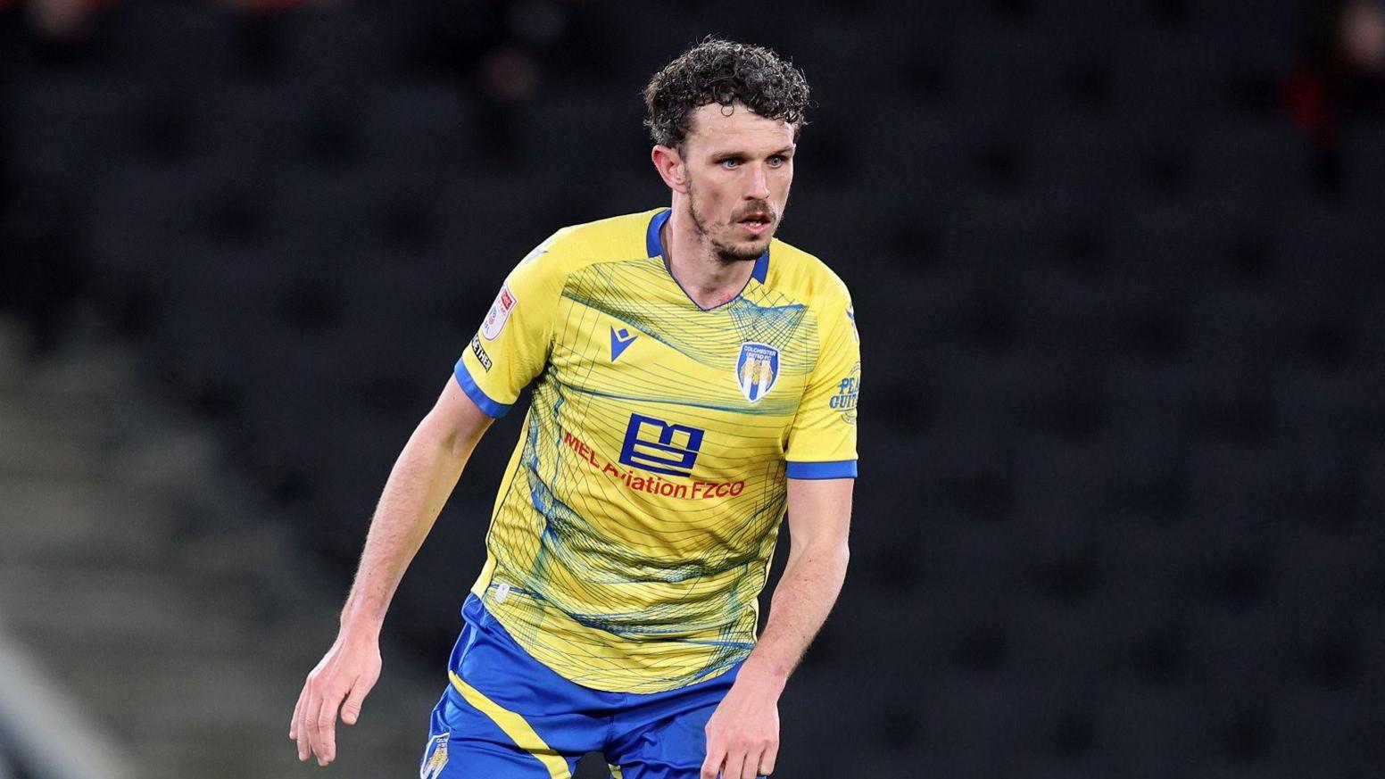 A photo of Tom Flanagan playing for Colchester United in their yellow and blue kit against former team MK Dons in March.