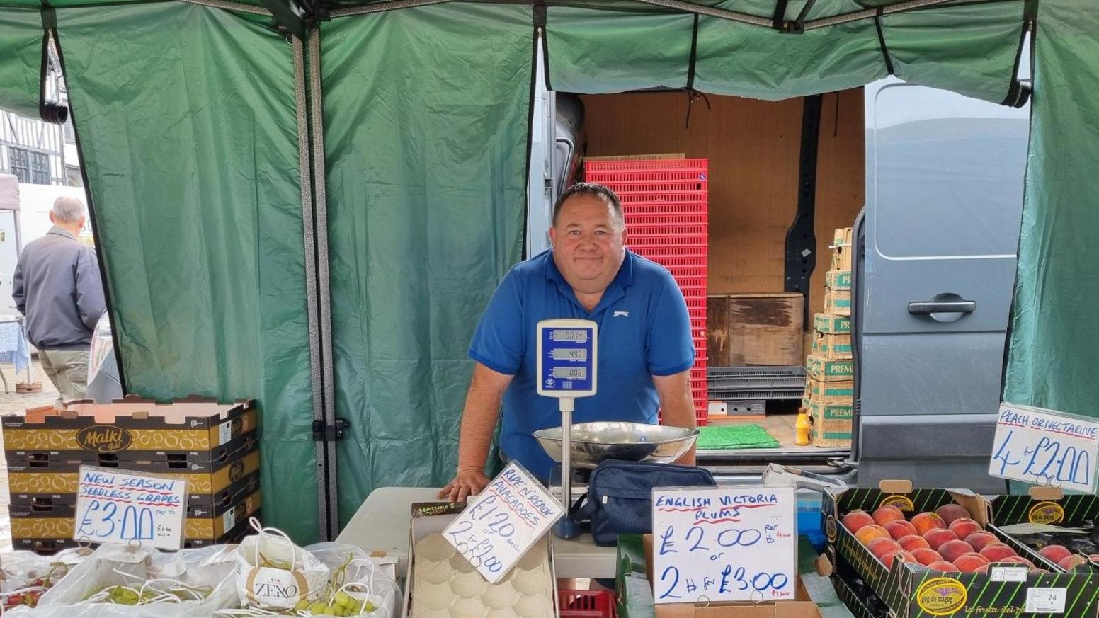 Brian Murphy is standing behind a stall of fruit and vegetables beneath a green gazebo