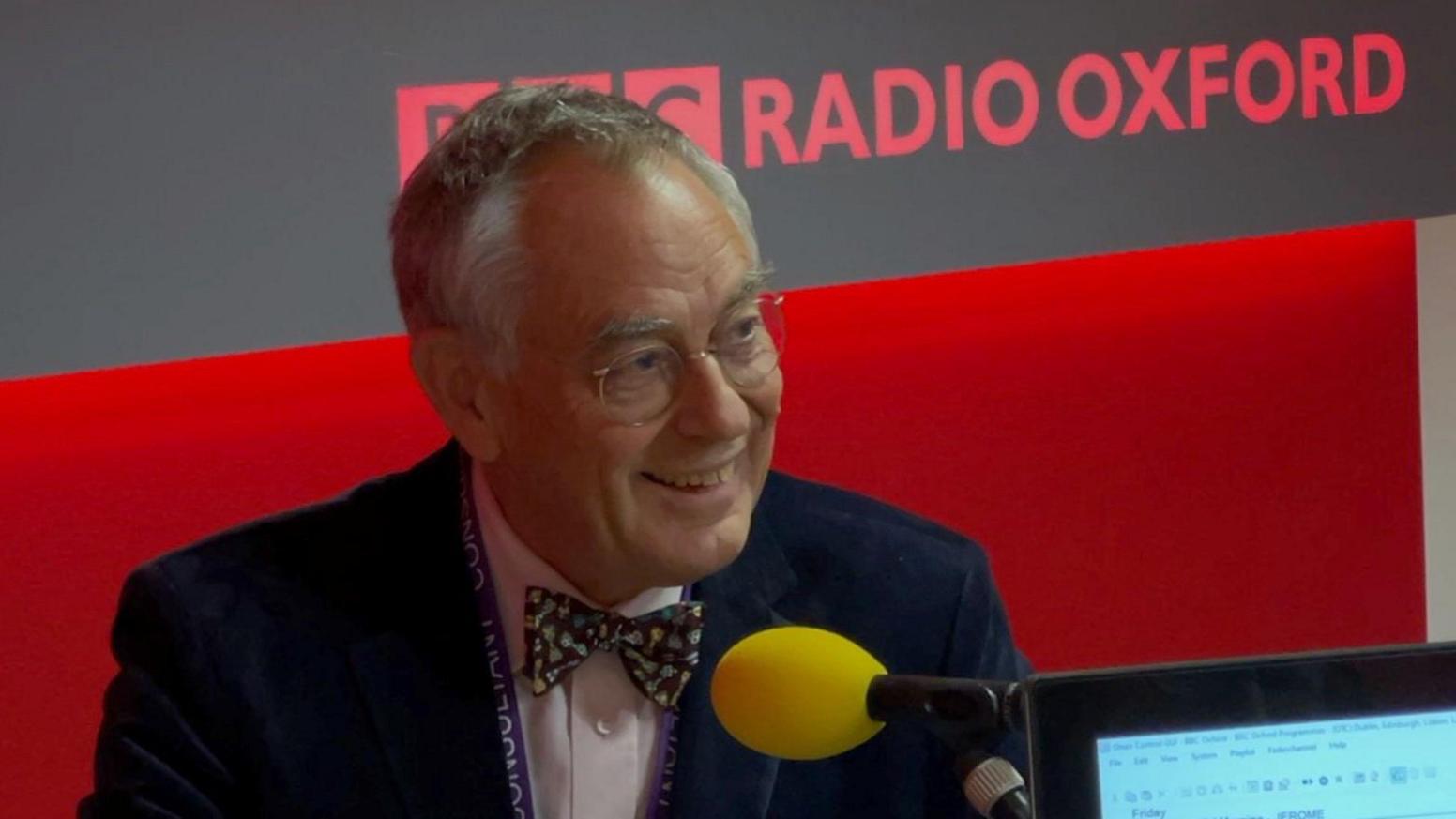 Dr Kevin Ives being interviewed at BBC Radio Oxford. He is looking away from the camera, smiling. There is a microphone with a yellow muff in front of him.