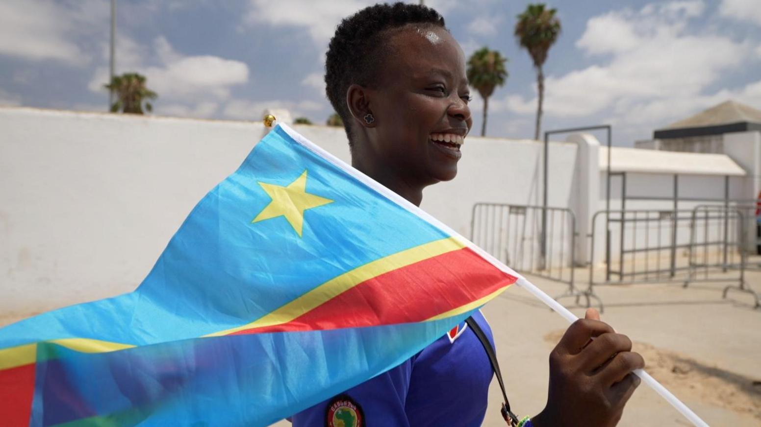 A DR Congo fan waves the country's flag on a white stick outside with white wall of a football stadium at the Women's Africa Cup of Nations
