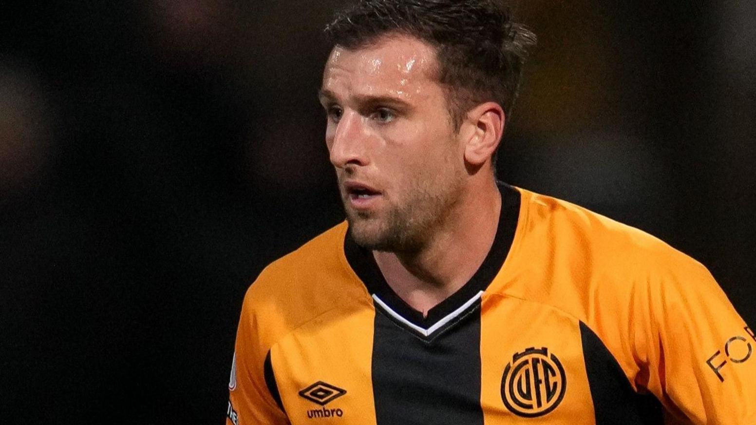 Footballer Ben Purrington playing for Cambridge United, wearing a black and gold striped shirt.