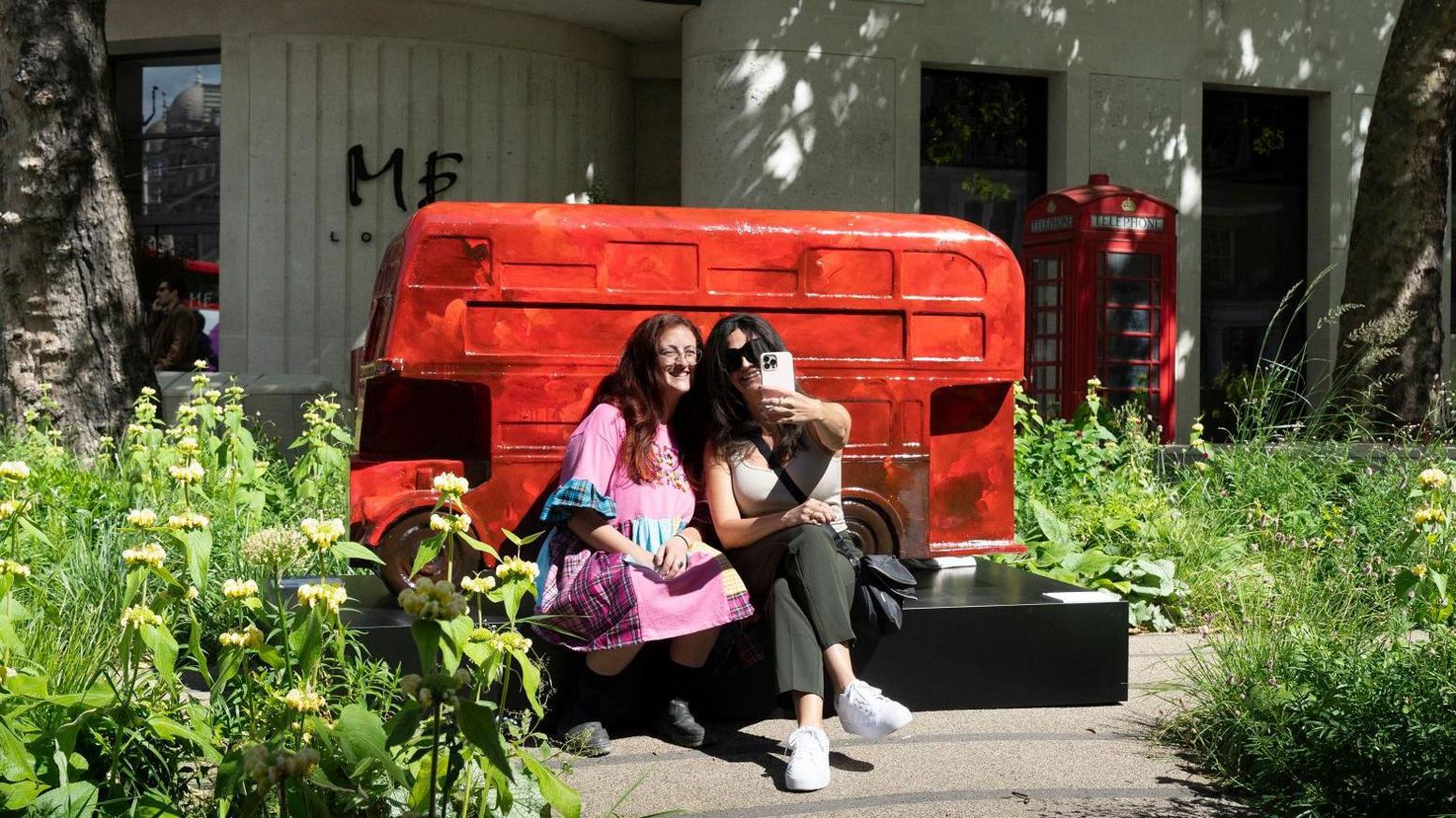 Two women taking a selfie in front of a London bus sculpture