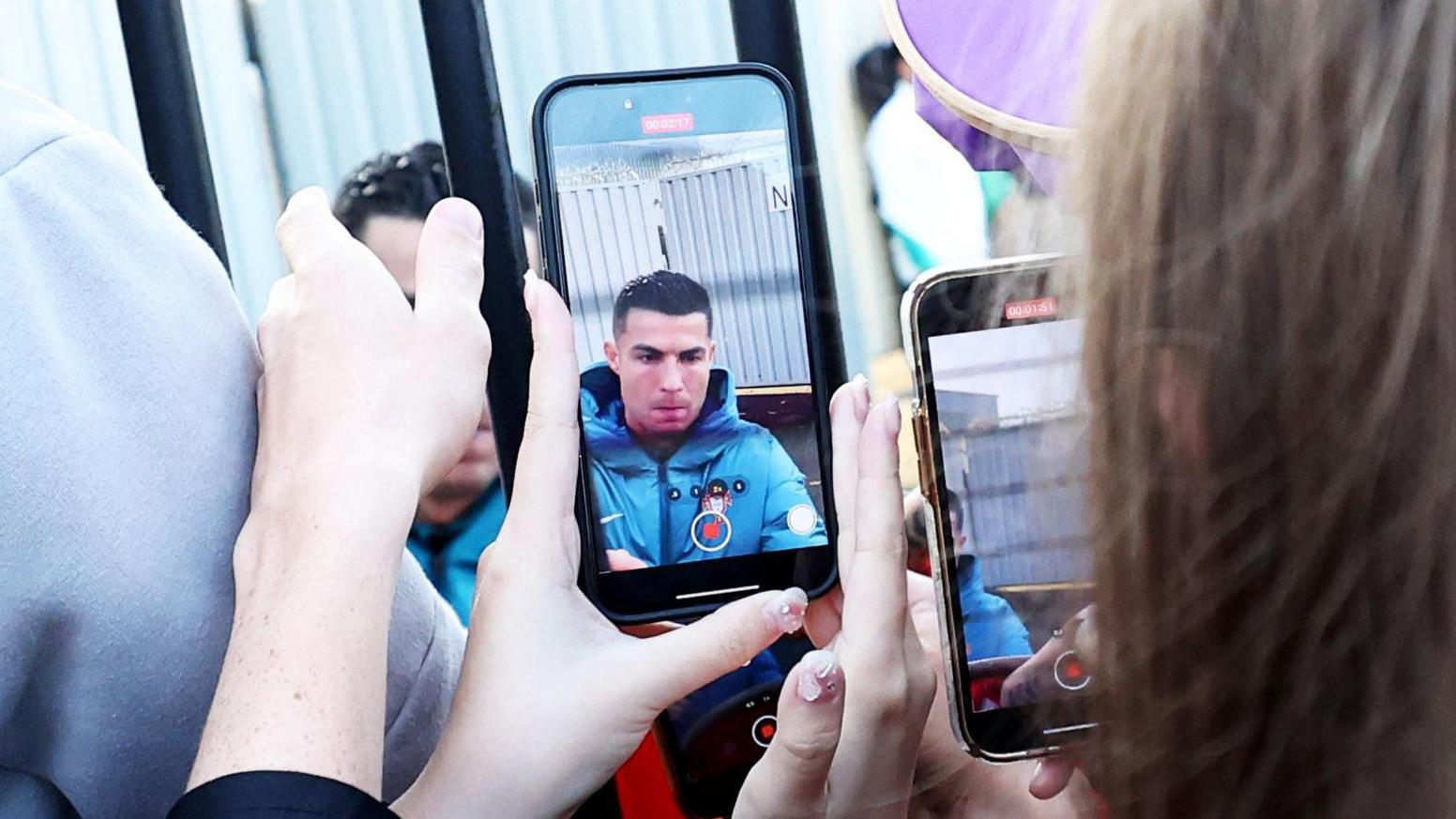 Cristiano Ronaldo can be seen through the lens of a phone signing items for fans at the St Mirren FC gates.