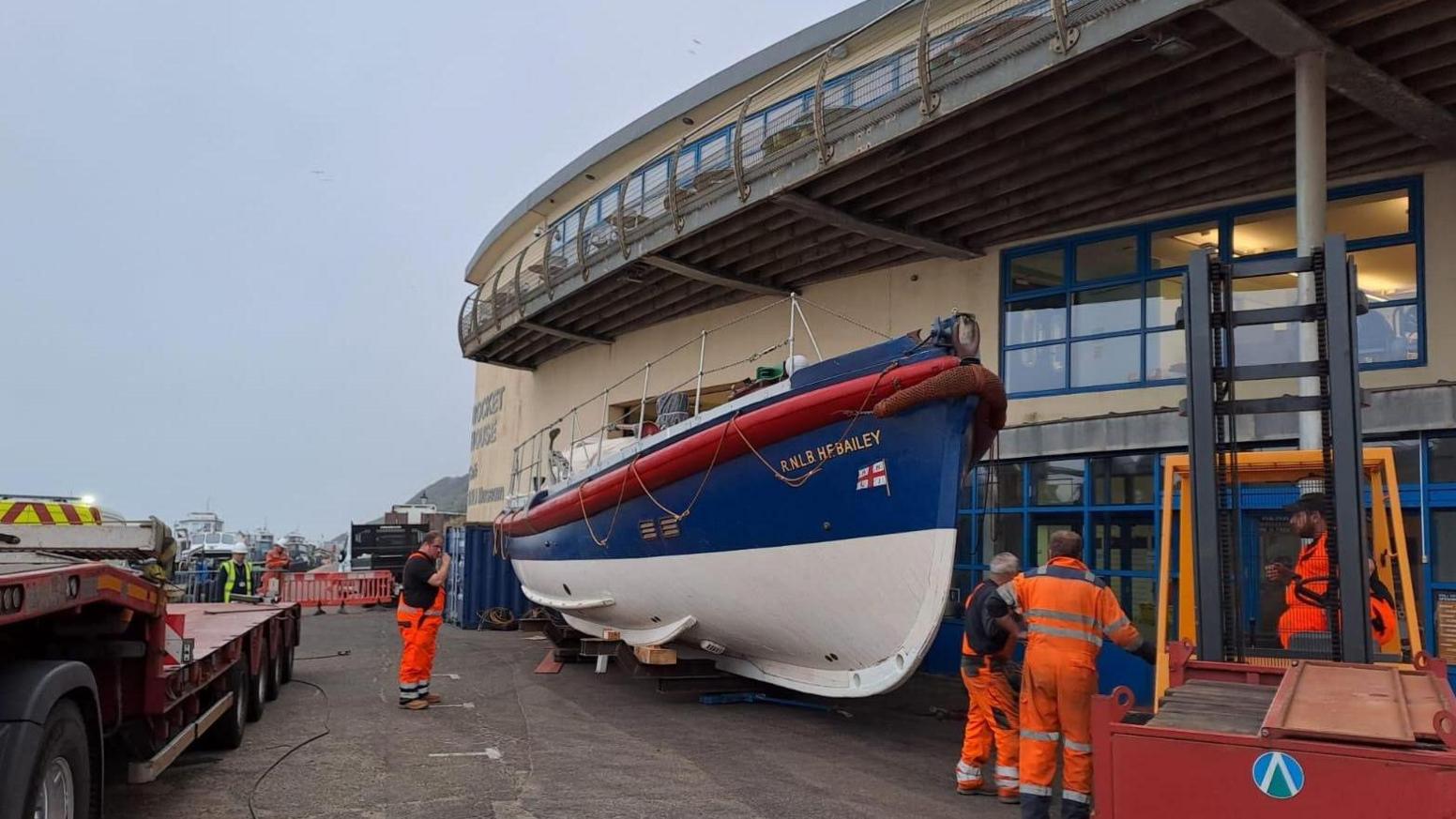 H F Bailey lifeboat and men in hi-vis workwear outside The Rocket House in Cromer 