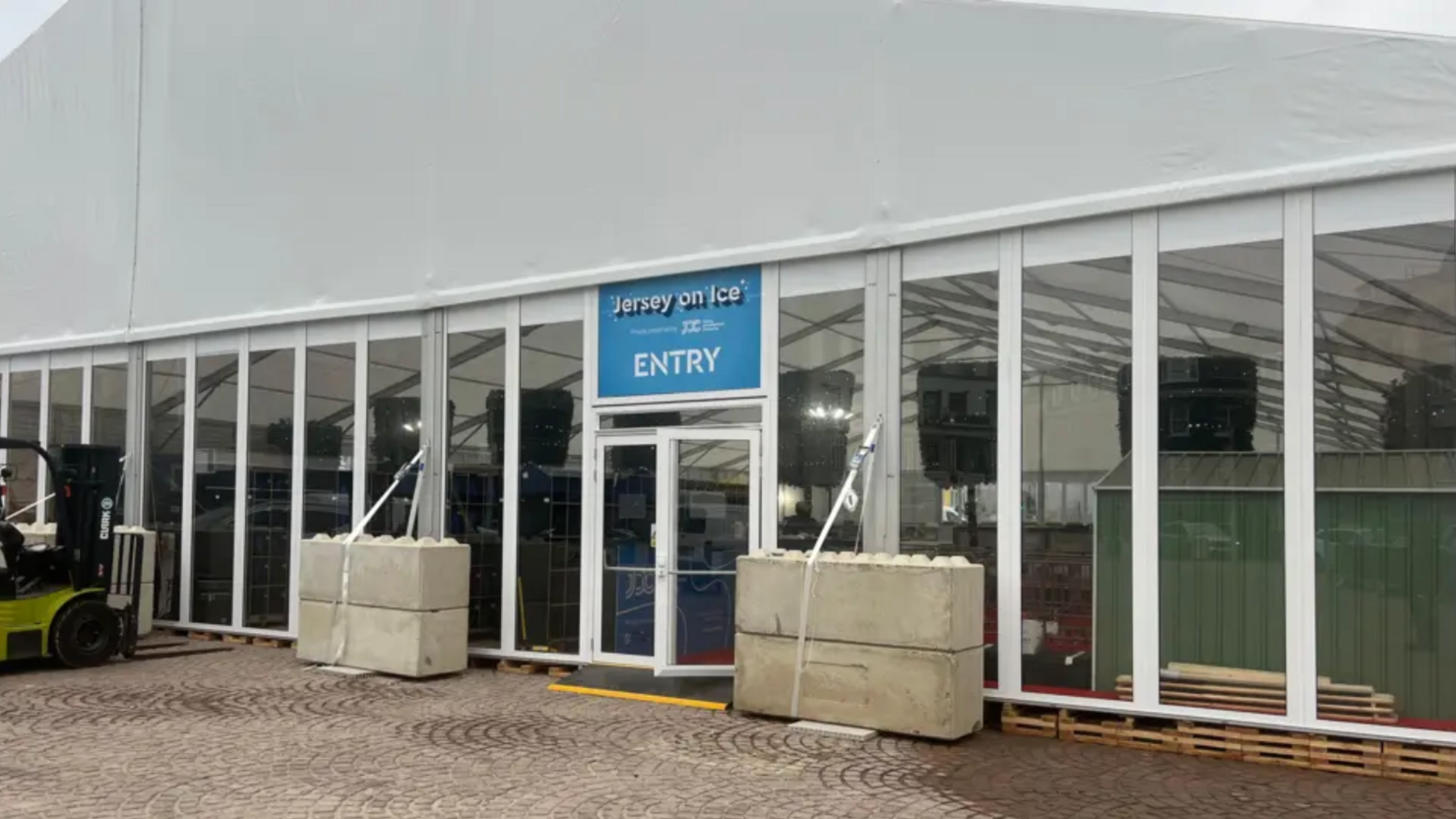 Jersey on Ice ice rink at St Helier entrance. A big white marquee is covering the ice rink. Transparent windows are all around the marquee. A large blue entry sign is above the door.