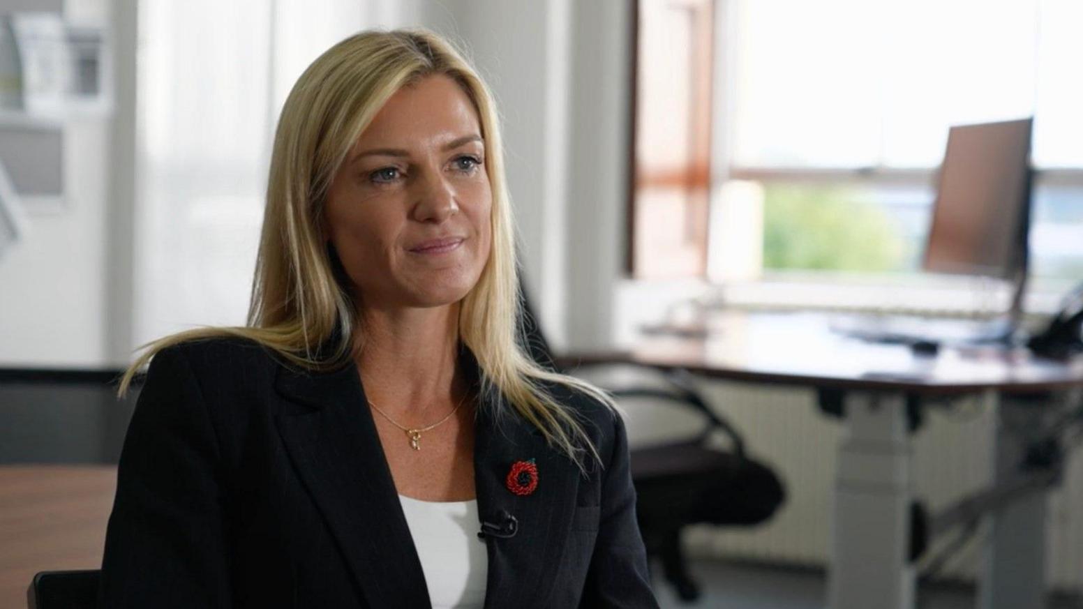 Det Ch Supt Alison Hurst with blonde hair, wearing a poppy and a jacket in a room with a desk and table in the background